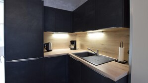 A modern kitchen with dark cabinets, a wooden countertop, a stainless steel sink, a coffee maker, and a paper towel dispenser. - Maison cosy proche mer (Créances)
