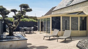 A covered patio area with a table and chairs, a fire pit, and a glass-enclosed structure. - Maison cosy proche mer (Créances)