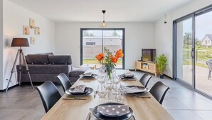 Un comedor con una mesa dispuesta para seis personas, un sofá, una lámpara, un televisor y un ventanal corredizo que da a un área exterior.