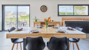 A dining area with a wooden table set for four, surrounded by black chairs. A vase with flowers is on the table, and a clock is on the wall. - Cozy home in Saint Germain sur Ay with WiFi (Saint Germain sur Ay)
