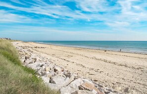Une plage de sable bordée de rochers, avec un ciel bleu dégagé.
