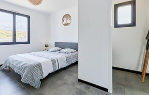 Quarto com cama, mesa de cabeceira, abajur, decoração de árvore na parede e janela.