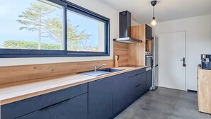 Una cocina moderna con un amplio ventanal, muebles oscuros y un refrigerador de acero inoxidable.