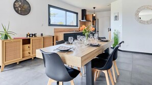 Un comedor moderno con una mesa de madera dispuesta para seis comensales, sillas negras y una cocina al fondo.