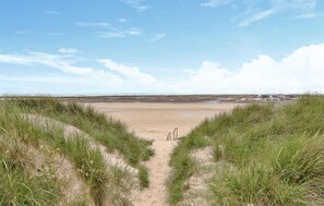 Ein sandiger Strand mit klarem Himmel und grasbewachsenen Dünen.