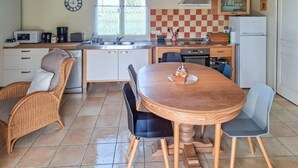 Una cucina con un tavolo rotondo in legno, sedie in vimini, uno schienale a scacchi e un frigorifero.