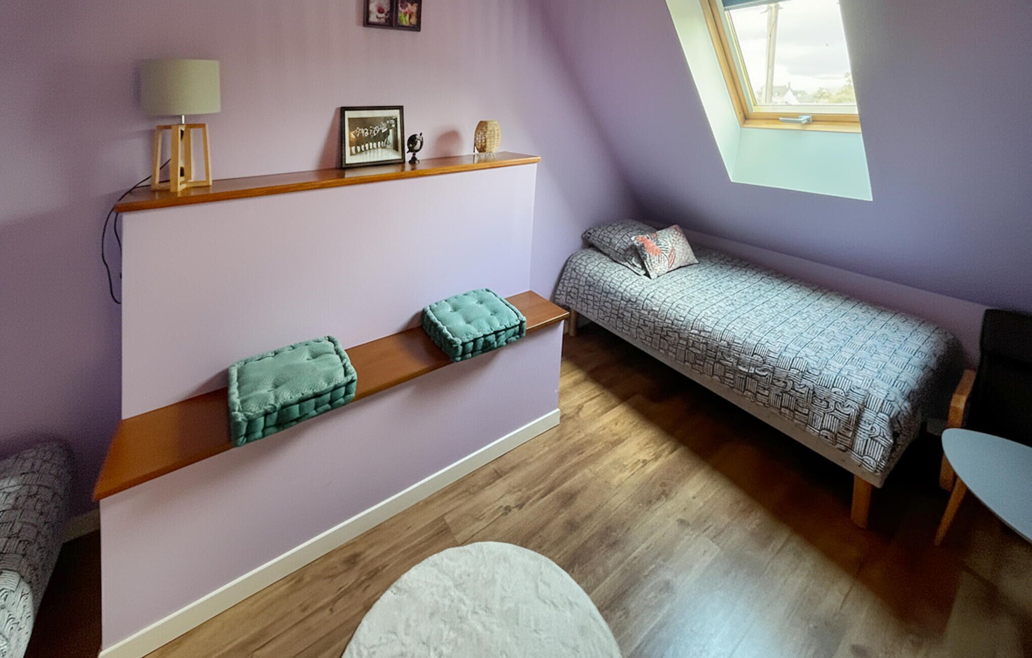Une chambre avec un lit en mezzanine, un petit bureau, une fenêtre et une étagère où sont disposés des objets décoratifs.