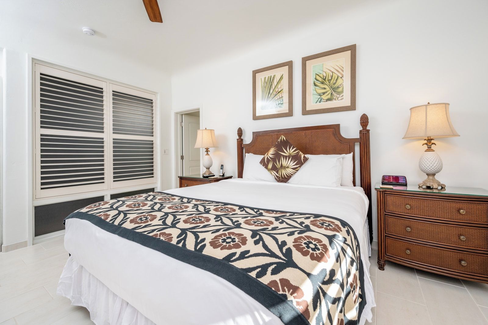 A hotel room with a large bed, two bedside lamps, a wooden nightstand, and a window with blinds.