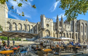 A historic building with arched windows and towers, surrounded by outdoor seating areas with umbrellas. - Beautiful home in Cabannes (Cabannes)