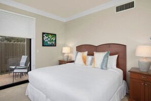 A hotel room with a large bed, two bedside tables with lamps, a painting on the wall, and a view of a patio with chairs. - Kapalua Bay | Ocean View 6 BR, Sleeps 20 | Car Incl. w/ 6+ Nights | KBV ML-2056 by KBM (Lahaina)