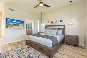 A bedroom with a bed, bedside tables, a ceiling fan, a TV, and framed pictures on the wall. - Kapalua Bay | Ocean View 6 BR, Sleeps 20 | Car Incl. w/ 6+ Nights | KBV ML-2056 by KBM (Lahaina)