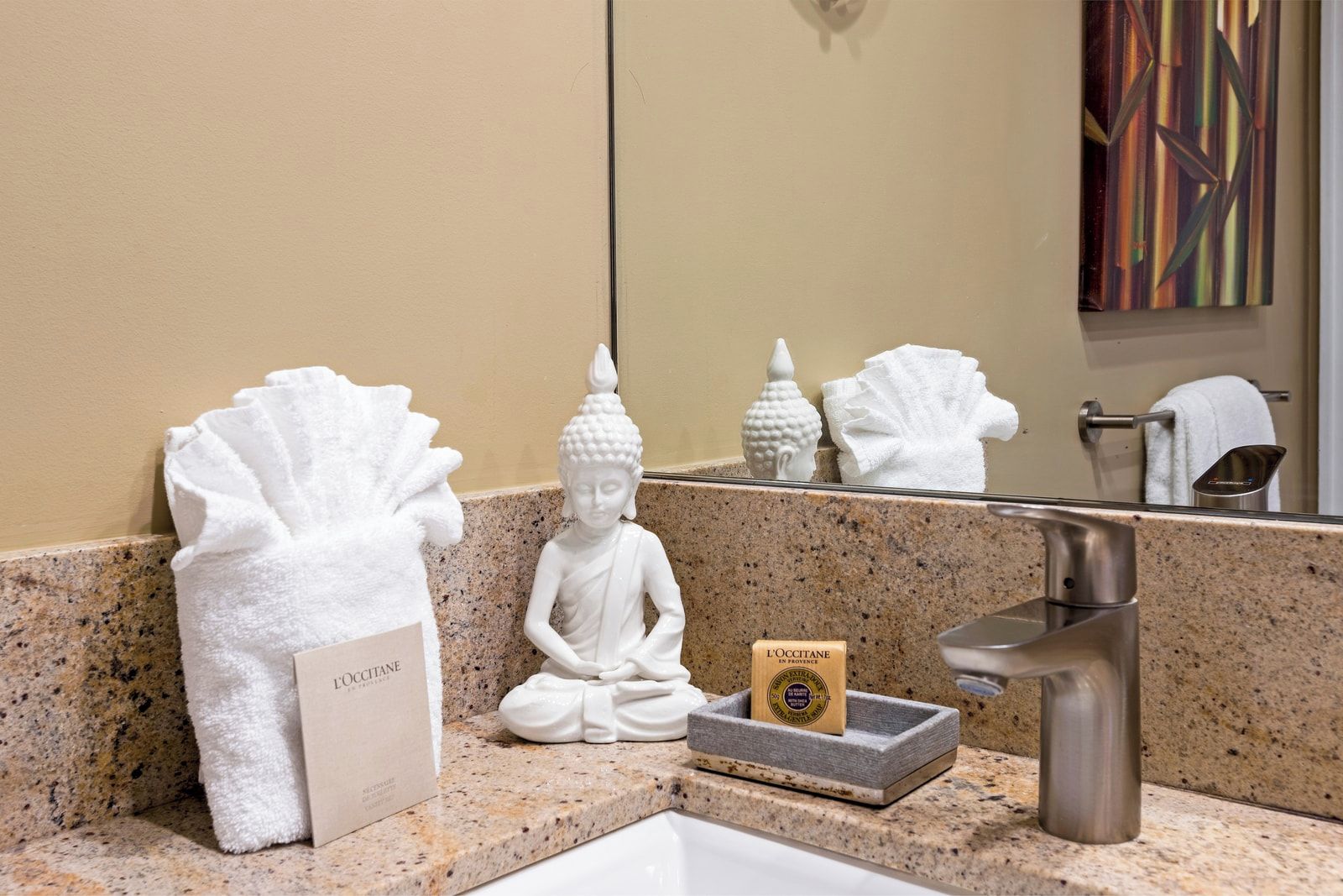Et badeværelse med en bordplade i granit, en hvid Buddha-figur, et håndklæde og en sæbeskål med etiket.