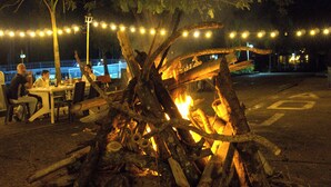 Un feu de camp avec des bûches et des briques, entouré de guirlandes lumineuses et de palmiers.