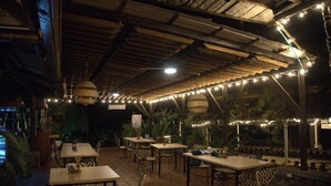 An outdoor patio area with tables and chairs, string lights, and potted plants. - Ecohotel El Castillo Pance (Cali)