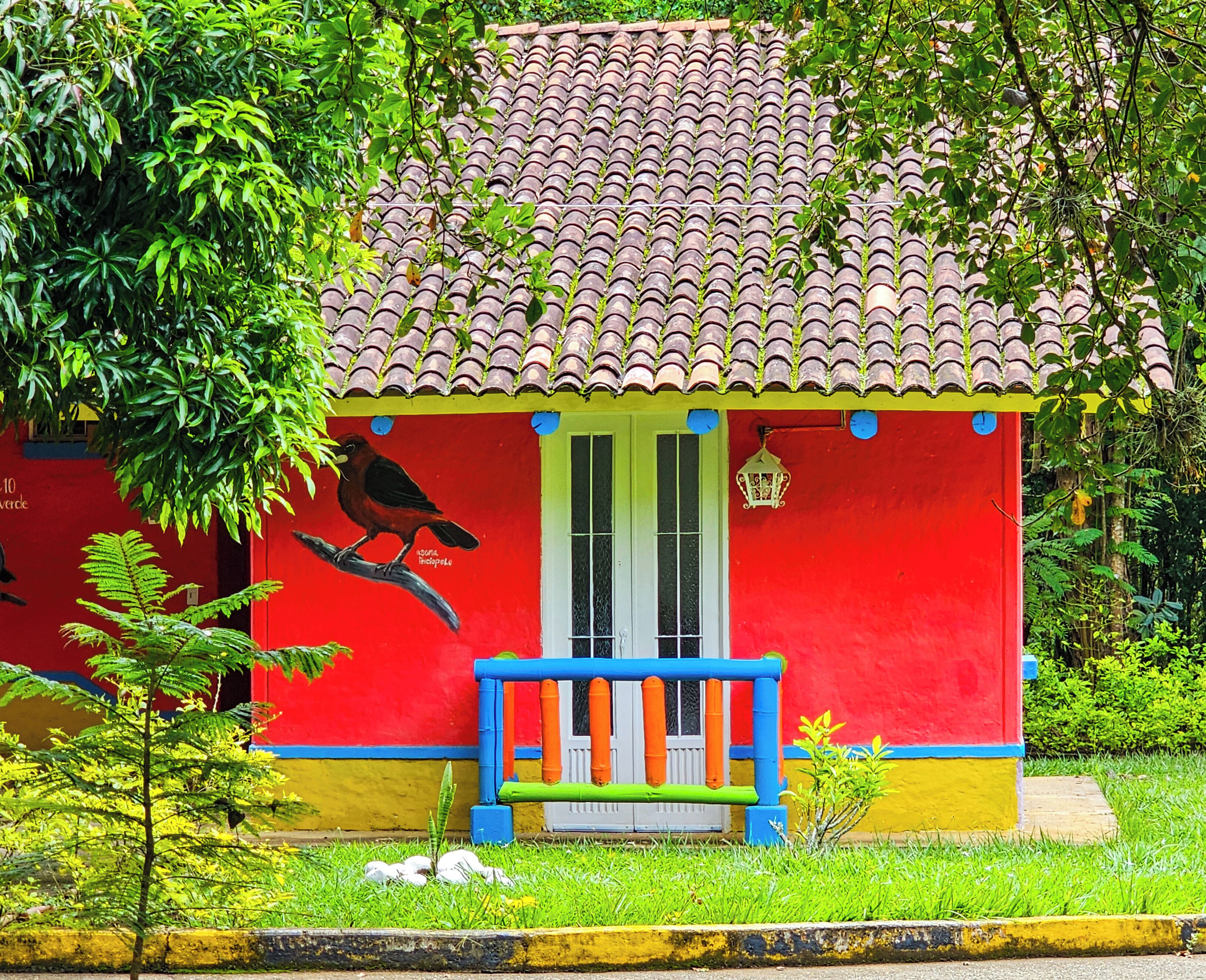 Una casa colorida con techo de tejas, puerta roja y barandilla azul.