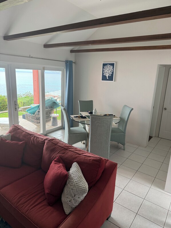 A living room with a red sofa, a dining table with chairs, and a view of the sea through a glass door. - Private pool and private beach in this wonderful Warwick beachfront apartment (Warwick Parish)