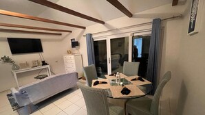 A dining area with a glass table, chairs, and a sofa. There is a TV on the wall and a window with curtains. - Private pool and private beach in this wonderful Warwick beachfront apartment (Warwick Parish)