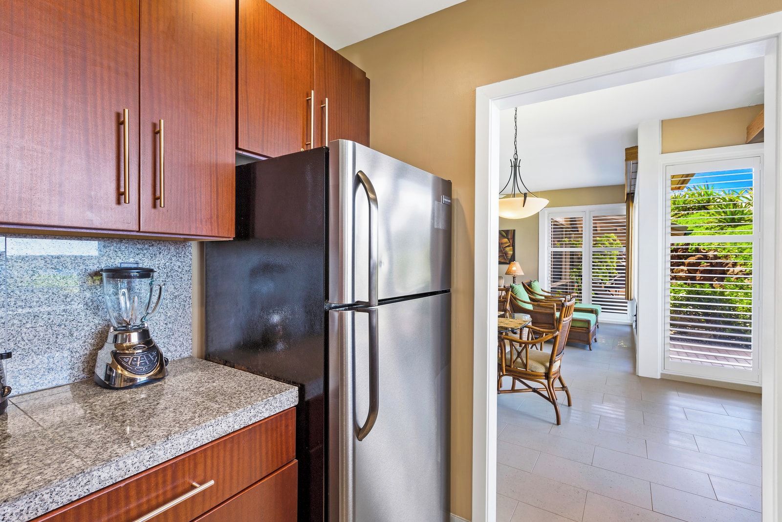 A kitchen with a stainless steel refrigerator, wooden cabinets, and a granite countertop.