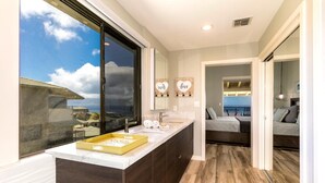 Un baño moderno con un ventanal grande, un tocador con un jabonera amarilla y vista al mar.