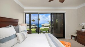Habitación de hotel con una cama grande, ventilador de techo, vista al océano y balcón con sillas.