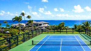 Una cancha de tenis con vista al océano y palmeras.