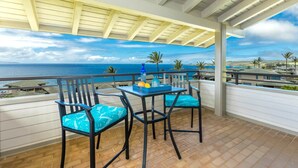 Un balcon avec vue sur l’océan, deux chaises, une table avec une bouteille et des fruits, et une pergola au-dessus.