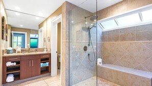 Une salle de bain moderne dotée d’une douche à parois de verre, de carreaux de marbre et d’un meuble-lavabo avec espace de rangement.