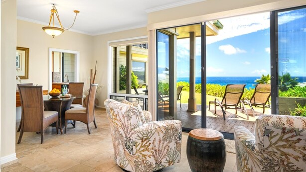 Una habitación amplia con comedor, un ventanal con vista al océano y un balcón con mobiliario exterior.