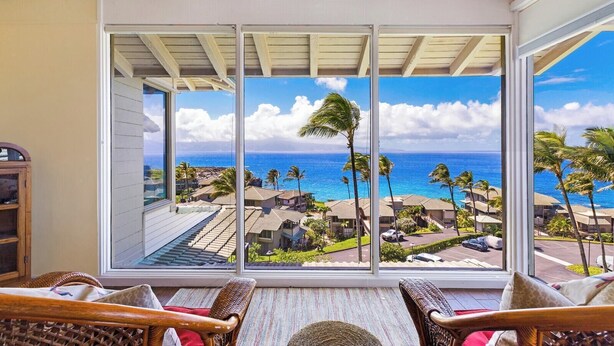 A room with a large sliding glass door leading to a balcony with a view of the ocean and palm trees. - Kapalua Bay | Ocean View 4 BR, Sleeps 14 | Car Incl. w/ 6+ Nights | KBV ML-2068 by KBM (Lahaina)