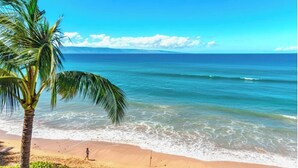 A beach with clear blue water, a palm tree, and a person walking on the sand. - Kapalua Bay | Ocean View 4 BR, Sleeps 14 | Car Incl. w/ 6+ Nights | KBV ML-2068 by KBM (Lahaina)
