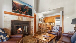 A cozy living room with a fireplace, leather sofas, a wooden coffee table, and a kitchen in the background. - Telluride Ski Getaway w/Fireplace, Hot-Tub & Pool (Mountain Village)
