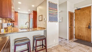 A kitchen with granite countertops, wooden cabinets, and two leather bar stools. - Kapalua Bay | Ocean View 4 BR, Sleeps 14 | Car Incl. w/ 6+ Nights | KBV ML-2062 by KBM (Lahaina)