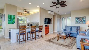 A spacious living area with a blue sofa, a coffee table, and a kitchen with a bar area. - Kapalua Bay | Ocean View 4 BR, Sleeps 14 | Car Incl. w/ 6+ Nights | KBV ML-2062 by KBM (Lahaina)
