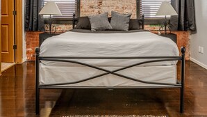Una camera da letto con una parete in mattoni, un letto con struttura in metallo, due abat-jour e una porta.