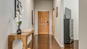Un corridoio con una porta in legno, una cassettiera nera e un vaso con fiori bianchi su un tavolo di legno.