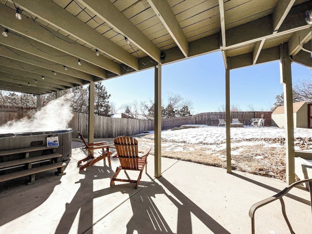 Eine überdachte Terrasse im Freien mit Whirlpool, Holzstühlen und Grill.