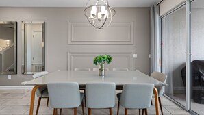 Un comedor moderno con una mesa grande, cuatro sillas, una araña y una planta.