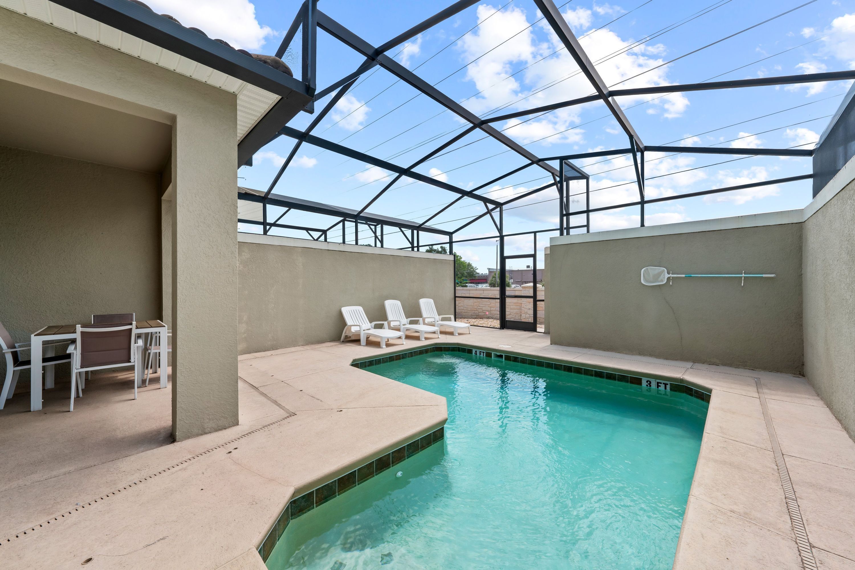 A covered outdoor swimming pool with lounge chairs and a table, surrounded by a metal frame structure.