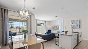 Una cocina moderna con una isla central, un comedor con mesa de vidrio y una sala de estar con sofá y sillas azules.