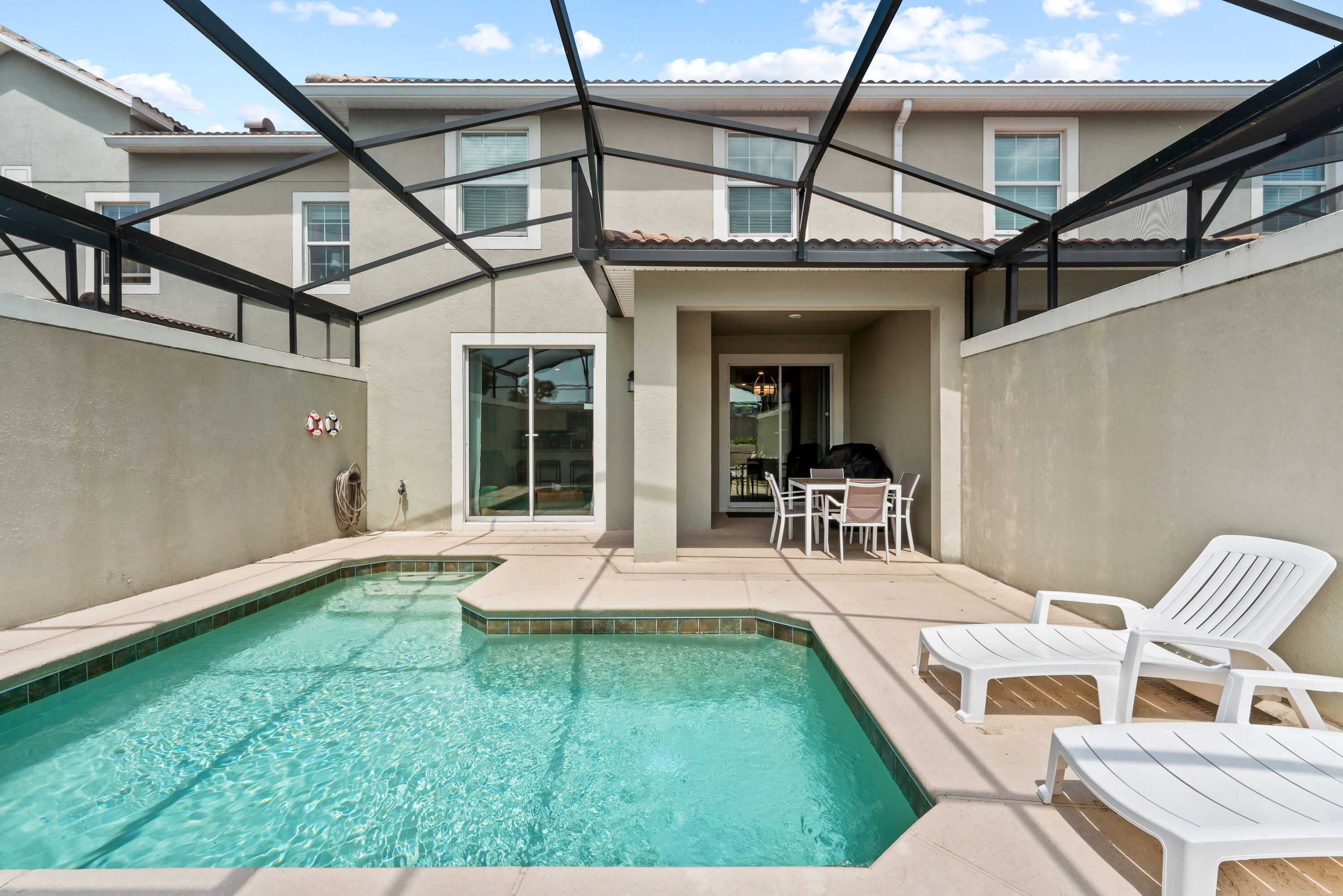 Ein Garten mit Swimmingpool, weißen Liegestühlen und einer überdachten Terrasse.