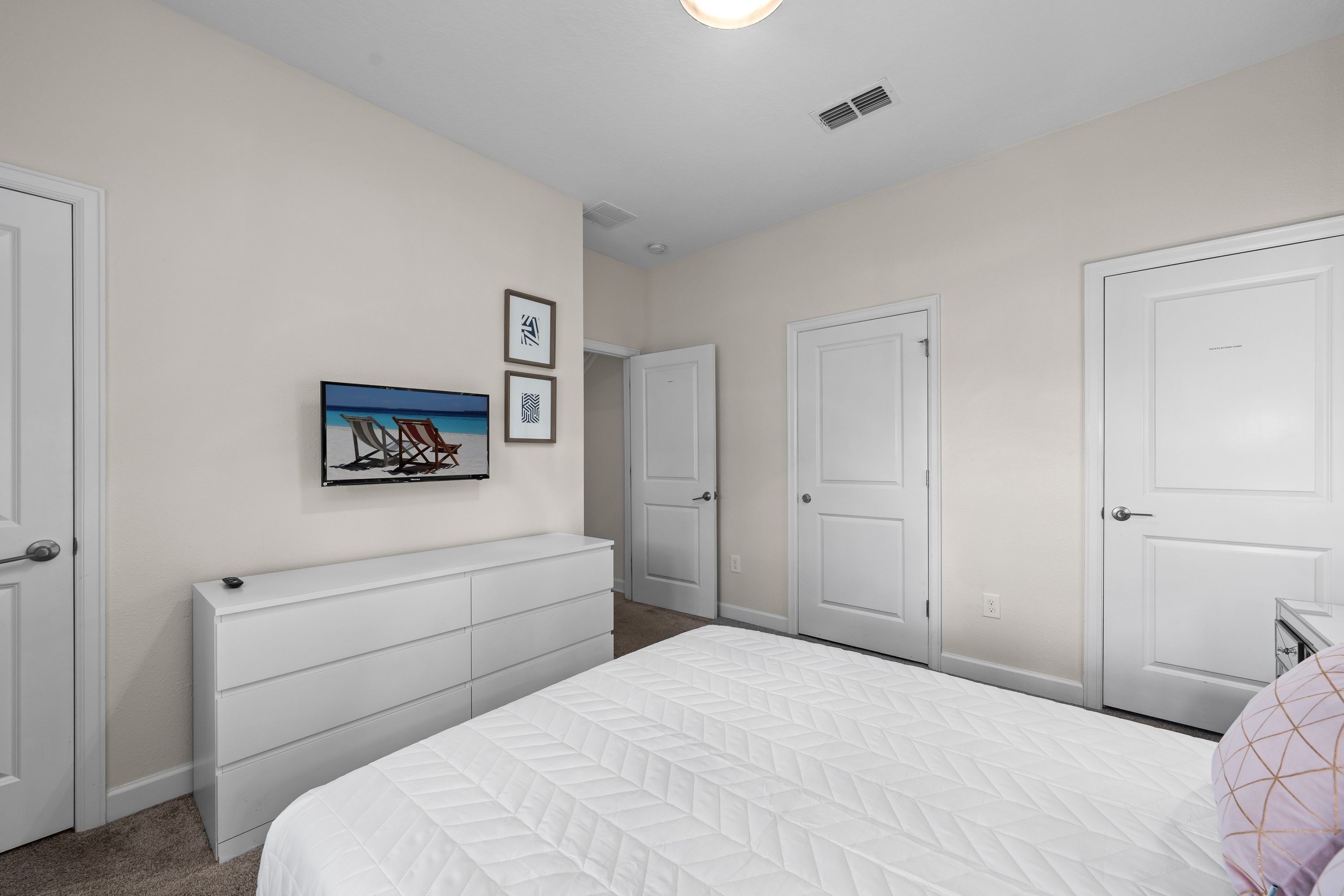 A bedroom with a bed, a dresser, and a door. There is a framed picture on the wall.