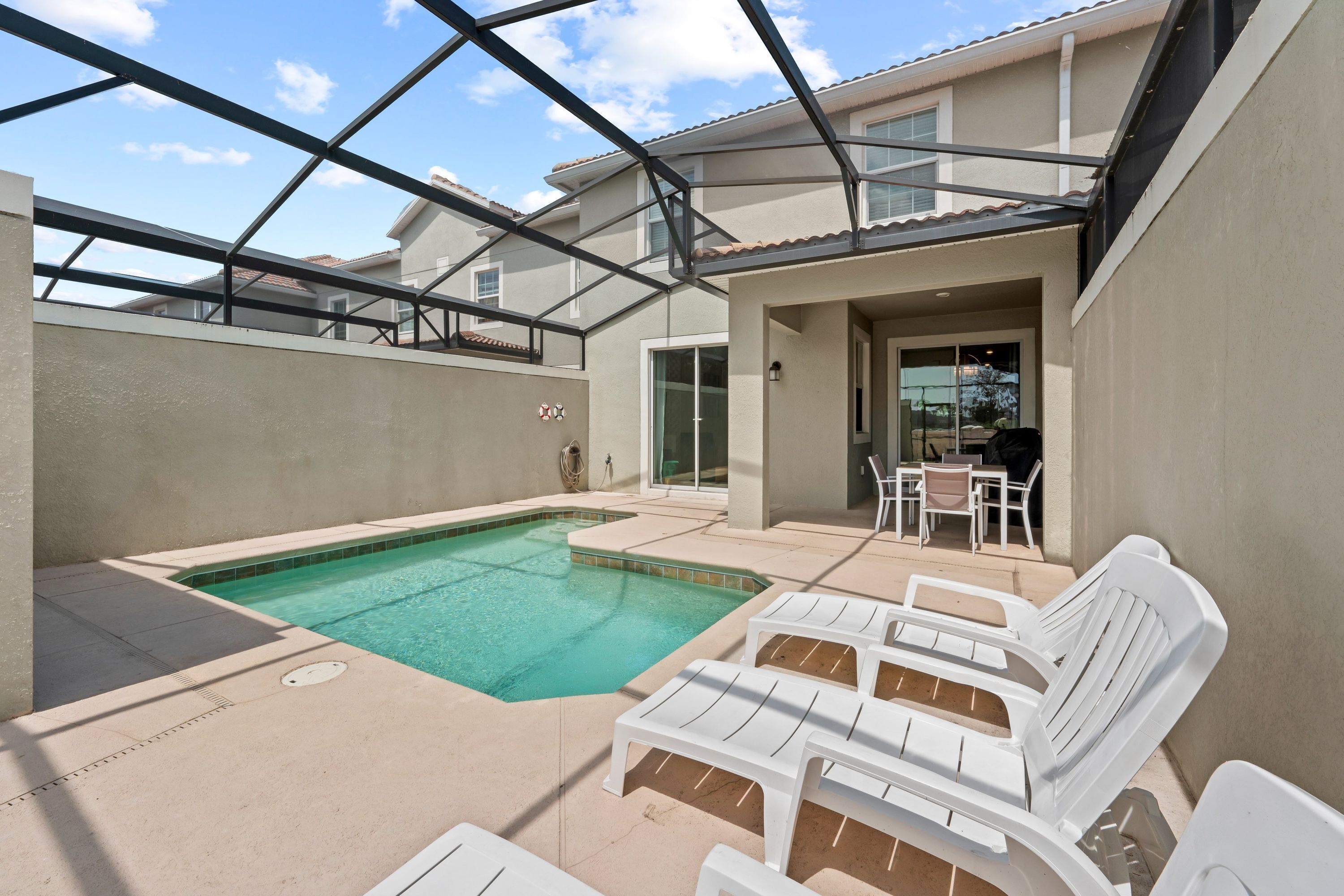 A swimming pool with lounge chairs, a covered patio, and a glass-enclosed area with a view of the sky.