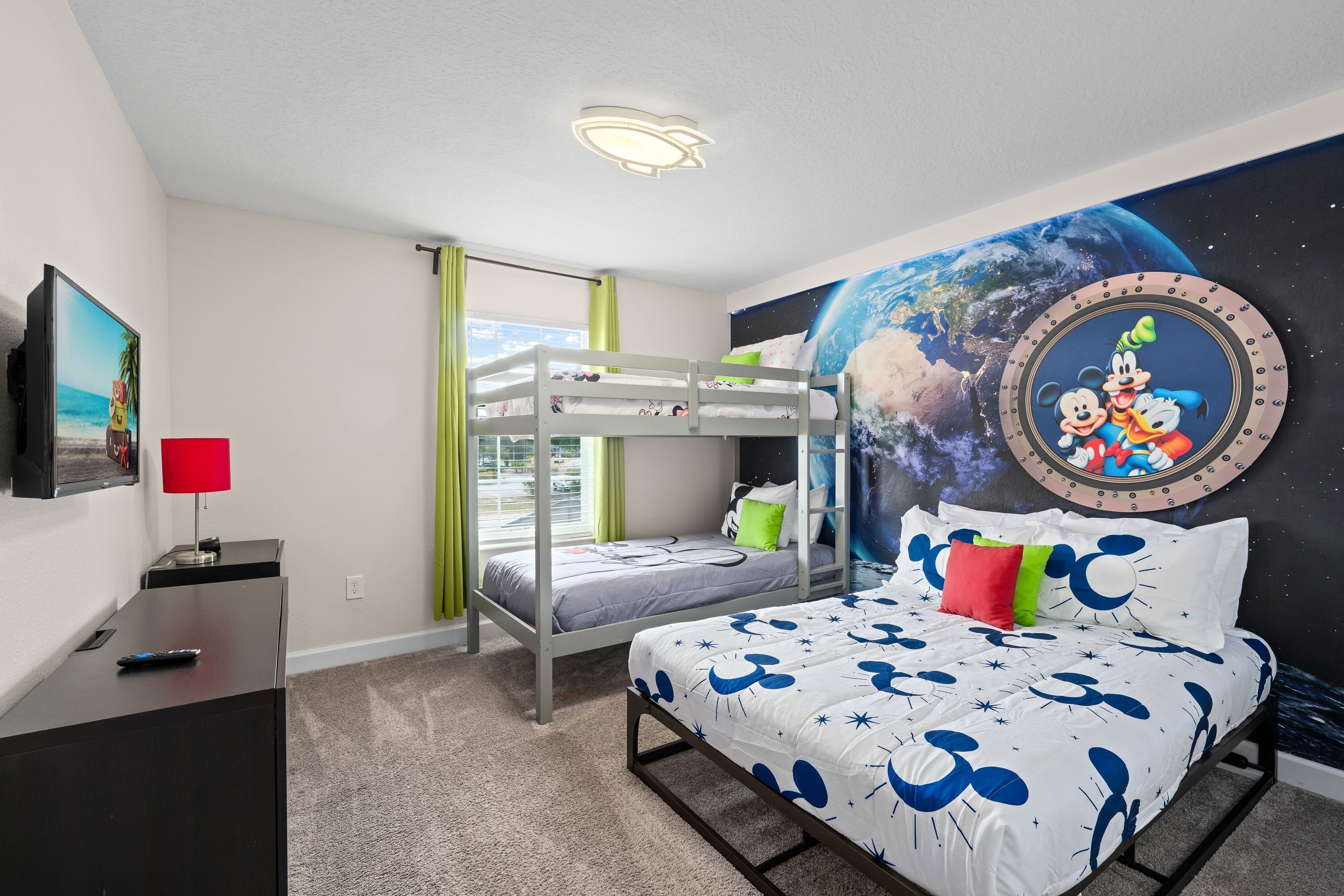A room with bunk beds, a desk with a lamp, a TV, and a mural of Mickey Mouse.