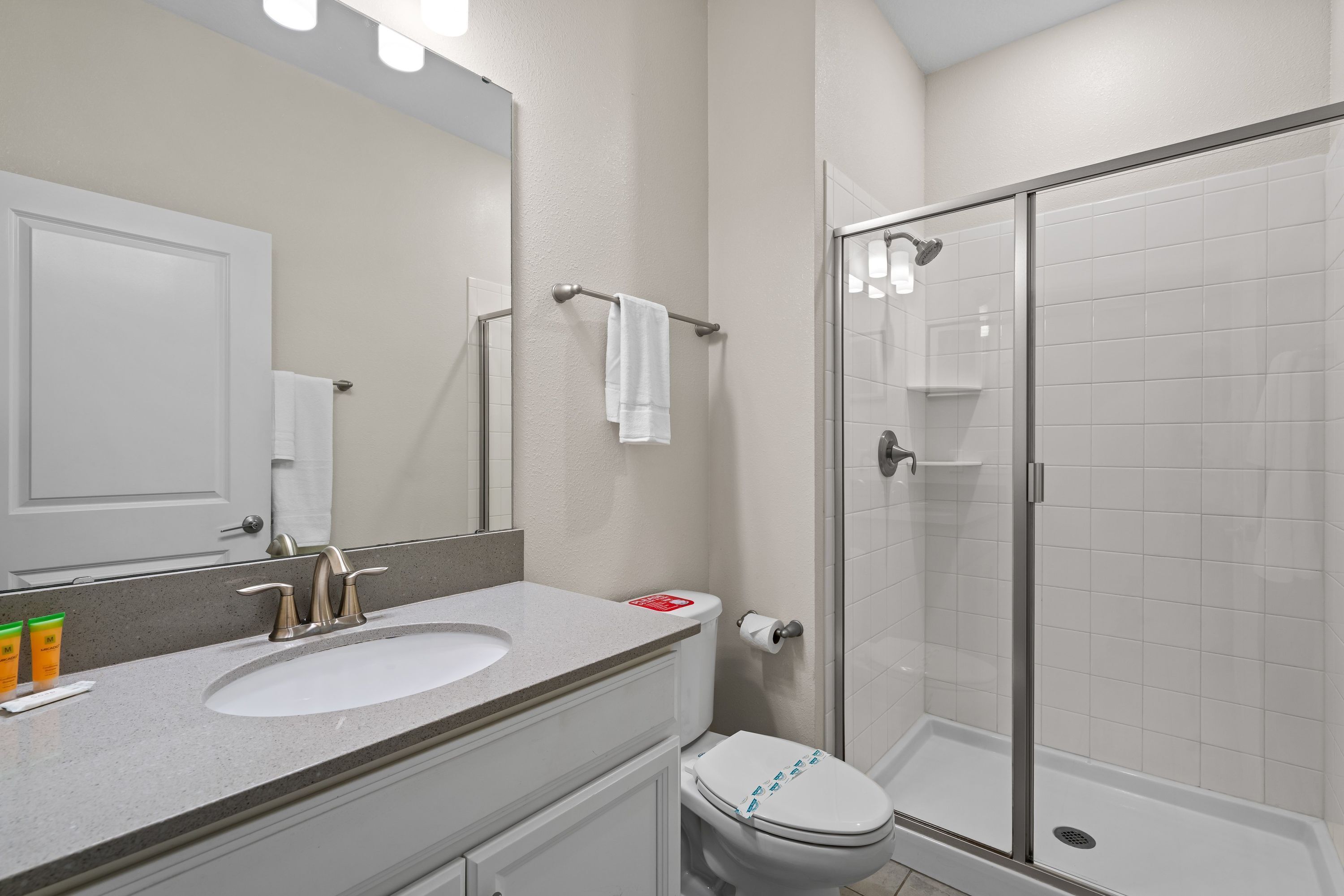 Une salle de bain avec un lavabo, un miroir et des toilettes blancs, ainsi qu’une douche séparée par une paroi de verre.