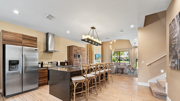 A modern kitchen with a stainless steel refrigerator, wooden cabinets, and a central island with bar stools. - Bright and Modern Townhome at Magic Village - Superb Disney Location (Kissimmee)