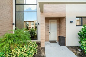 A modern building entrance with a large glass window, a door labeled "308", and a small trash bin to the right. - Bright and Modern Townhome at Magic Village - Superb Disney Location (Kissimmee)