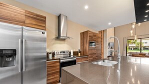 A modern kitchen with stainless steel appliances, wooden cabinets, and a large island with a sink. - Bright and Modern Townhome at Magic Village - Superb Disney Location (Kissimmee)