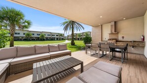 A spacious outdoor patio with a sofa, dining table, and grill area, overlooking a well-maintained lawn and buildings. - Bright and Modern Townhome at Magic Village - Superb Disney Location (Kissimmee)