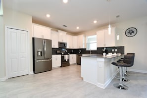 A modern kitchen with white cabinets, stainless steel appliances, and a bar area with stools. - Modern Oasis Near Shopping n Golf Course w Pool (Davenport)