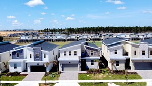 A residential area with modern houses featuring garage doors, well-maintained lawns, and a clear sky. - Modern Oasis Near Shopping n Golf Course w Pool (Davenport)